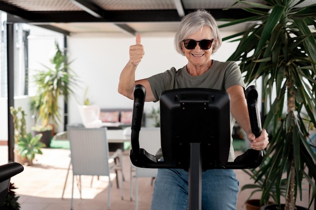People sport concept Smiling senior woman on stationary bike doing exercises on patio at home