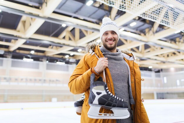 people, sport and leisure concept - happy young man with ice-skates on skating rink