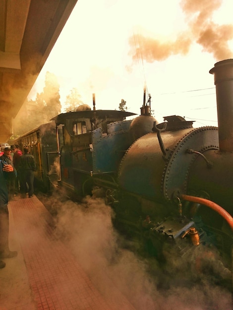 鉄道駅のプラットフォームで蒸気列車のそばに立っている人々