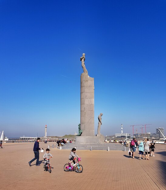 People at statue against clear blue sky