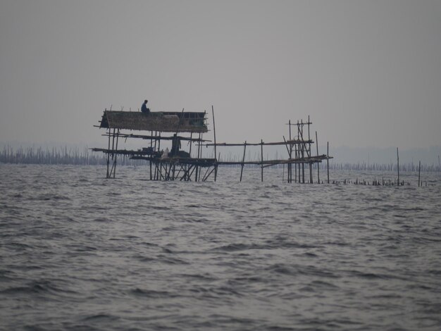 Photo people at stilt house in sea against clear sky