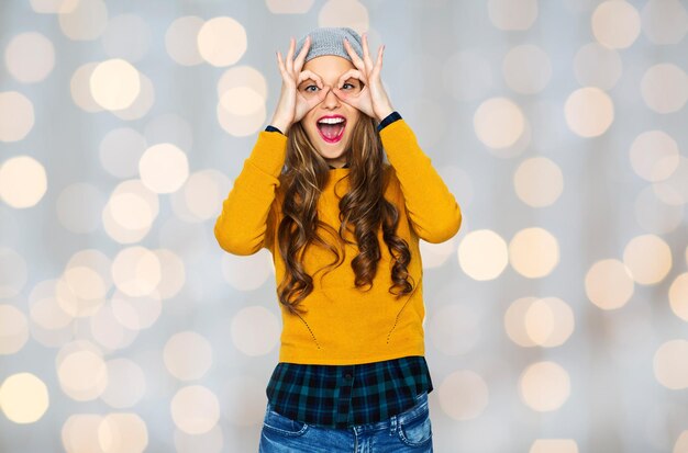 People, style and fashion concept - happy young woman or teen girl in casual clothes and hipster hat having fun over holidays lights background