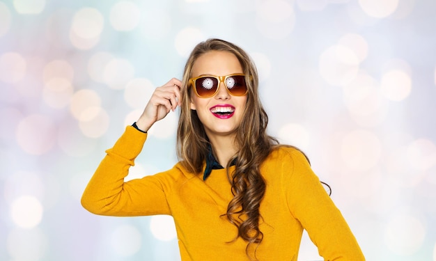 people, style and fashion concept - happy young woman or teen girl in casual clothes and sunglasses over holidays lights background