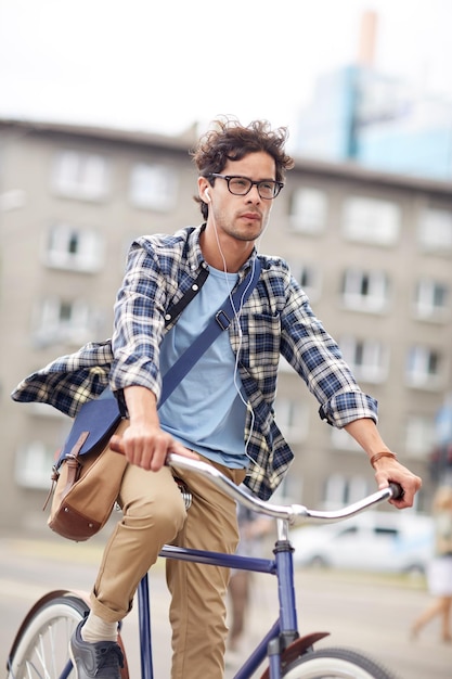 people, style, leisure and lifestyle - young hipster man with shoulder bag and earphones riding fixed gear bike on city street