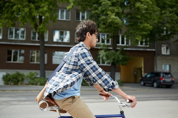 people, style, leisure and lifestyle - young hipster man with shoulder bag riding fixed gear bike on city street