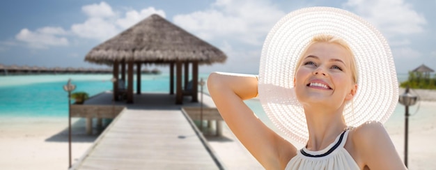 people, summer holidays, travel, tourism and vacation concept - beautiful woman in sun hat enjoying summer over maldives beach with bungalow background