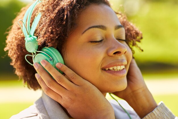 people, summer, technology and leisure concept - happy african american young woman face with headphones listening to music outdoors