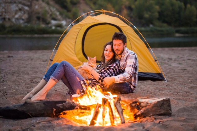 People, summer tourism and nature concept - couple near camp fire warming up seen from the tent.