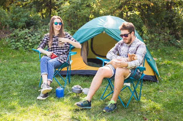 People, summer tourism and nature concept - young couple drinking tea near tent.