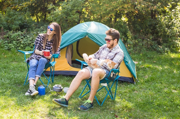 people, summer tourism and nature concept - young couple sitting near a tent