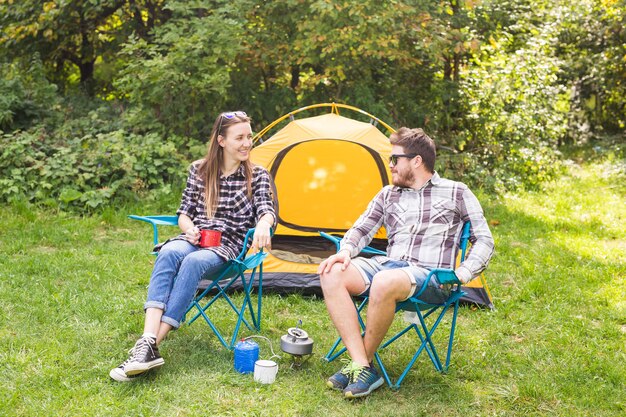 People, summer tourism and nature concept - young couple sitting near a tent.