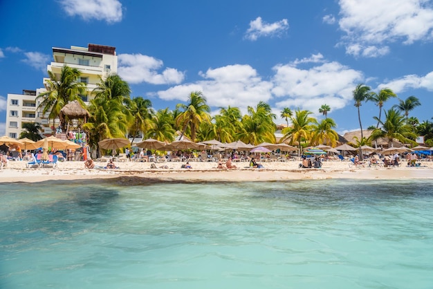 People sunbathing on the white sand beach with umbrellas\
bungalow bar and cocos palms turquoise caribbean sea isla mujeres\
island caribbean sea cancun yucatan mexico