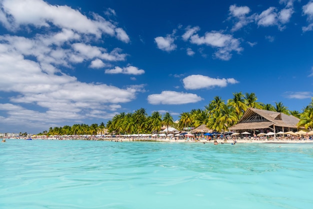 Люди загорают на белом песчаном пляже с зонтиками, бунгало, баром и кокосовыми пальмами, бирюзовое Карибское море, остров Исла Мухерес, Карибское море, Канкун, Юкатан, Мексика