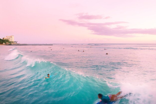 People surfing in sea against sky during sunset