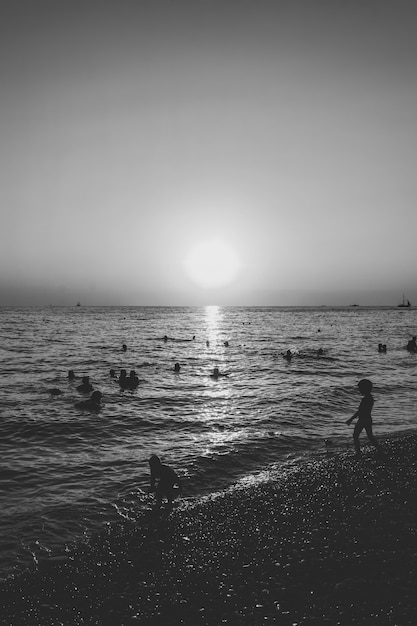 La gente nuota nel mare la sera al tramonto, foto in bianco e nero