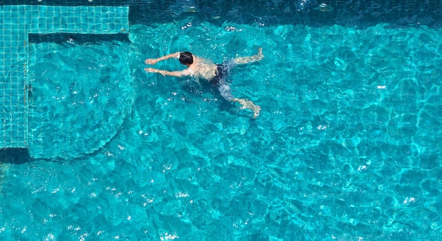 푸른 물과 태양 빛이 있는 호텔 수영장에서 수영하는 사람들은 그것에 반사되고 위쪽 시야각이 보입니다.