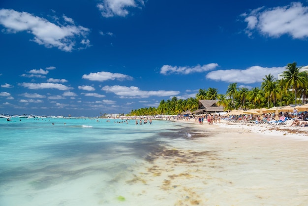 Люди плавают возле пляжа с белым песком с зонтиками, бунгало, баром и кокосовыми пальмами, бирюзовое Карибское море, остров Исла Мухерес, Карибское море, Канкун, Юкатан, Мексика