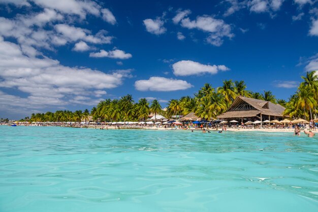 People swimming near white sand beach with umbrellas bungalow bar and cocos palms turquoise caribbean sea Isla Mujeres island Caribbean Sea Cancun Yucatan Mexico