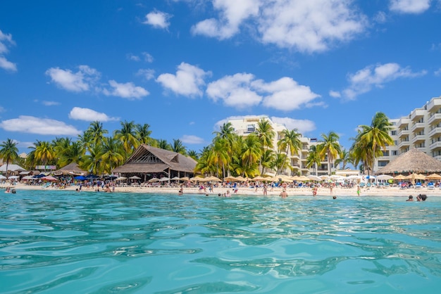 People swimming near white sand beach with umbrellas bungalow bar and cocos palms turquoise caribbean sea Isla Mujeres island Caribbean Sea Cancun Yucatan Mexico