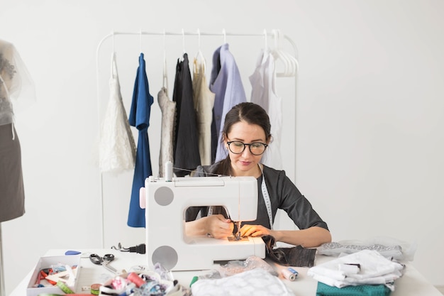 People, tailor, dressmaker and fashion concept - Smiling female fashion designer using sewing machine.