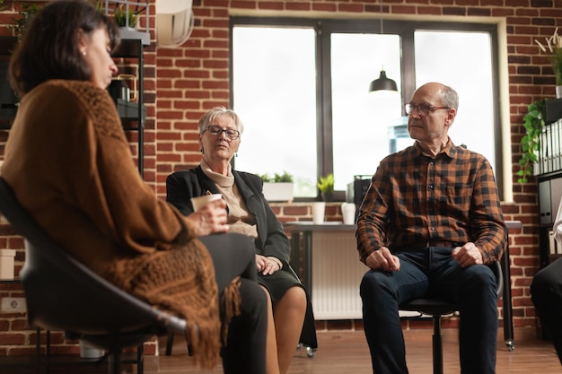 People talking to psychologist at aa group therapy session, sharing addiction problems. Multi ethnic patients having discussion about alcohol issues with specialist at support meeting program.