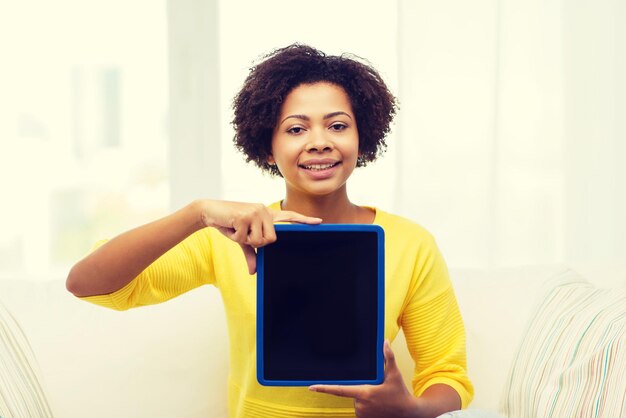 люди, технологии, реклама и концепция досуга - счастливая афроамериканская молодая женщина сидит на диване и показывает планшетный компьютер черный пустой экран дома