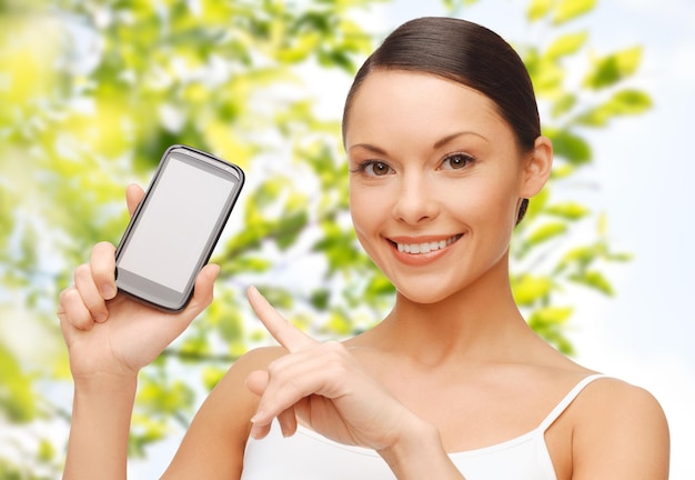 Photo people, technology, communication and internet connection concept - happy young woman pointing finger to smartphone blank screen over green tree leaves background