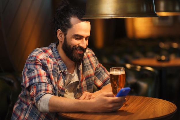 people and technology concept - happy man with smartphone drinking beer and reading message at bar or pub