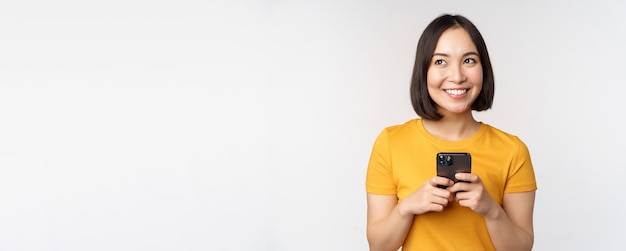 People and technology concept smiling asian girl using smartphone texting on mobile phone standing a