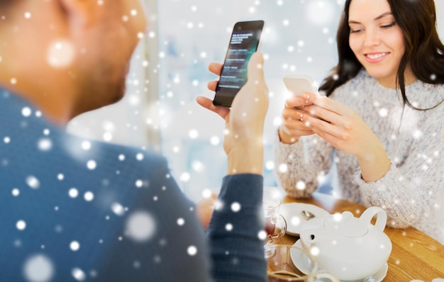 people, technology and dating concept - happy couple with smartphones drinking tea at cafe or restaurant