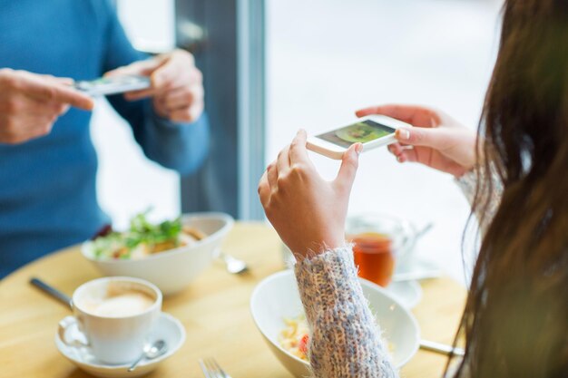 people, technology, eating and dating concept - close up of couple with smartphones picturing food at cafe or restaurant