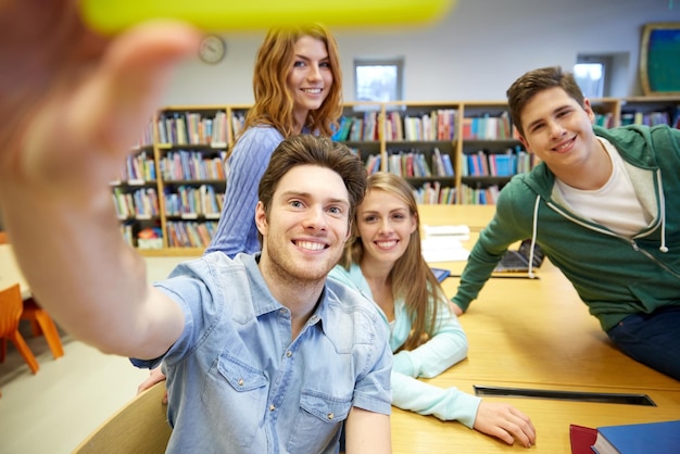 people, technology, education and school concept - happy students or friends with smartphone taking selfie in library