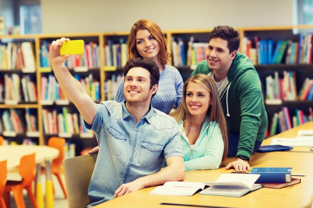 people, technology, education and school concept - happy students or friends with smartphone taking selfie in library