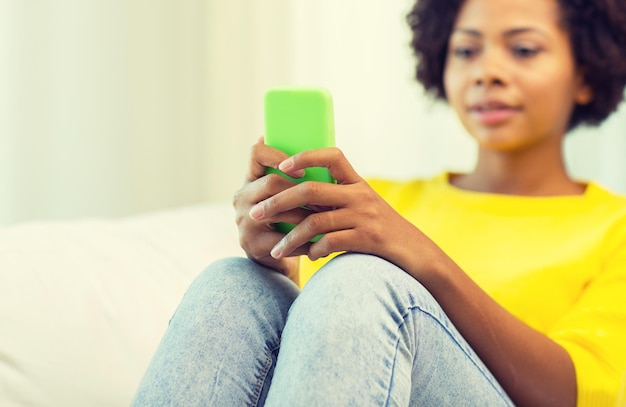 people, technology and leisure concept - close up of happy african american young woman texting on smartphone at home