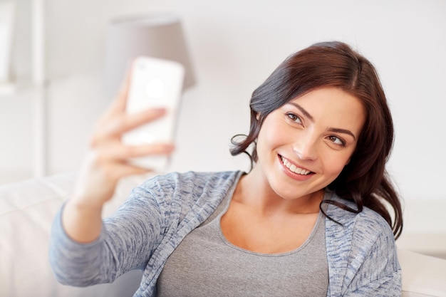 people, technology and leisure concept - happy woman taking selfie with smartphone at home
