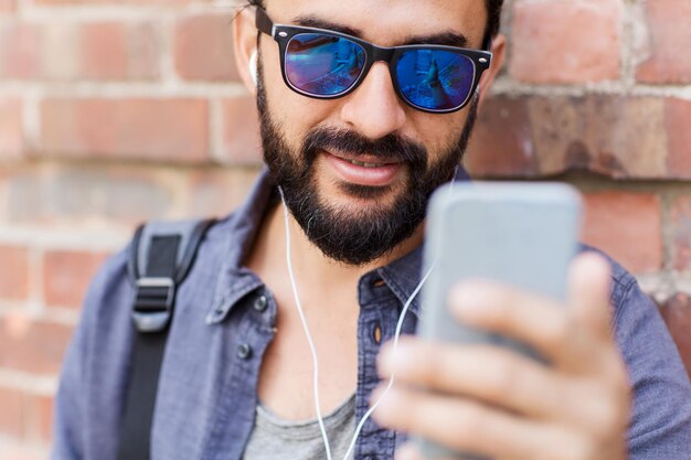 사람, 기술, 레저 및 라이프스타일 - 도시 거리에서 이어폰, 스마트폰, 가방을 들고 음악을 듣는 남자