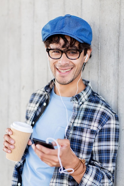 people, technology, leisure and lifestyle - man with earphones and smartphone drinking coffee and listening to music on city street