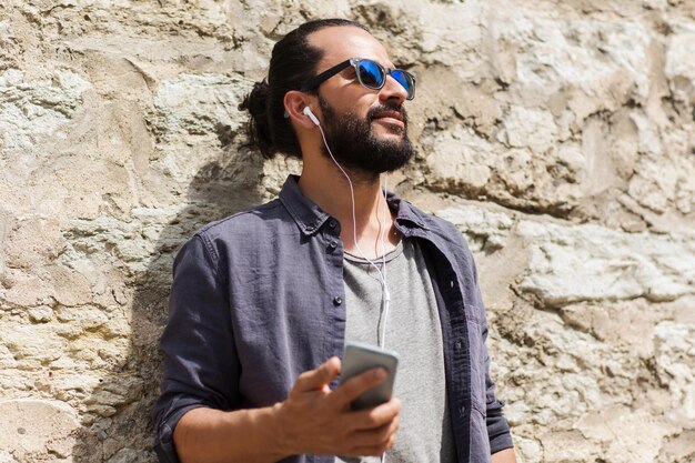 people, technology, leisure and lifestyle - man with earphones and smartphone listening to music on city street