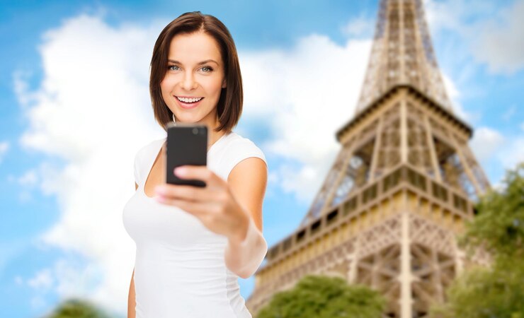 Photo people, technology, tourism and travel concept - young woman taking selfie with smartphone over paris eiffel tower background