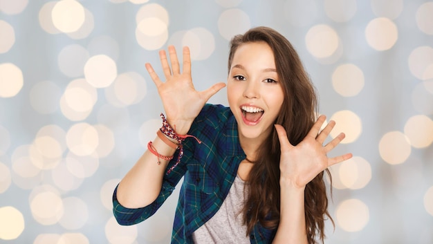 people and teens concept - happy laughing pretty teenage girl showing hands over holidays lights background