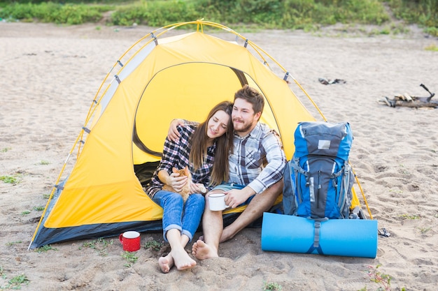 People, tourism and nature concept - Couple having fun on camping trip and play with cat.