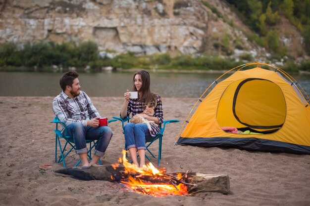 People, tourism and nature concept - Man and woman with their cat sit near a fire.