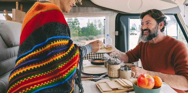 People in travel vacation leisure inside a camper van enjoying lunch together Man and woman with rent rv vehicle Happy caucasian couple in van life off grid day Nature outdoors outside the window