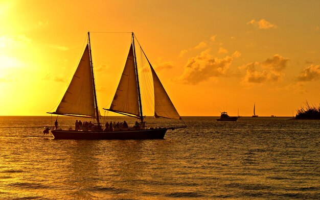 People traveling on sailboat against orange sky