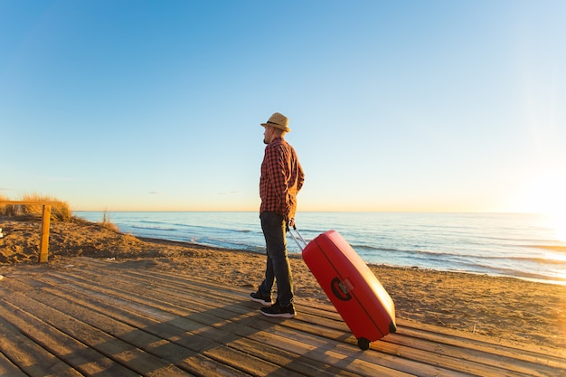 People, travelling and vacation concept - portrait of happy man walking by sea with suitcase.