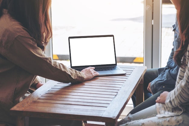 People using and looking at mockup laptop computer on wooden table together