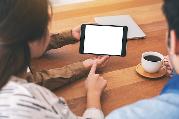 People using, looking and pointing at the same mockup tablet pc on wooden table together