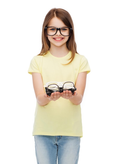 people and vision concept - smiling cute little girl in black eyeglasses holding many glasses in her hands