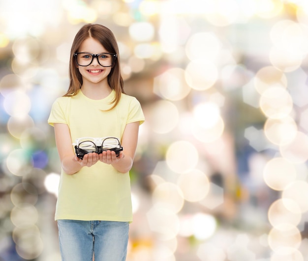 Photo people and vision concept - smiling cute little girl in black eyeglasses holding many glasses in her hands