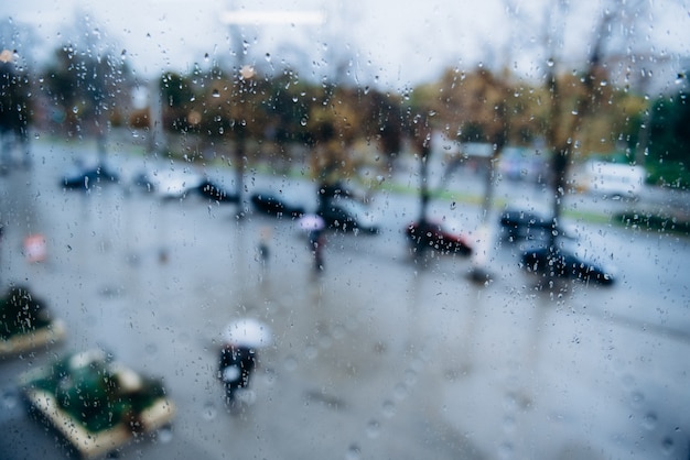 人々は通りを雨の中を歩き、濡れた窓から眺めます